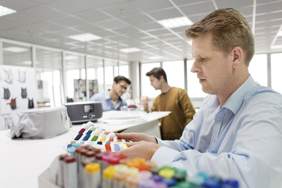 Mann betrachtet einen Farbfächer, im Hintergrund Produktmuster von Radios