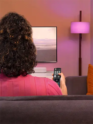 Person sitzt auf Sofa und steuert TV mit Fernbedienung.