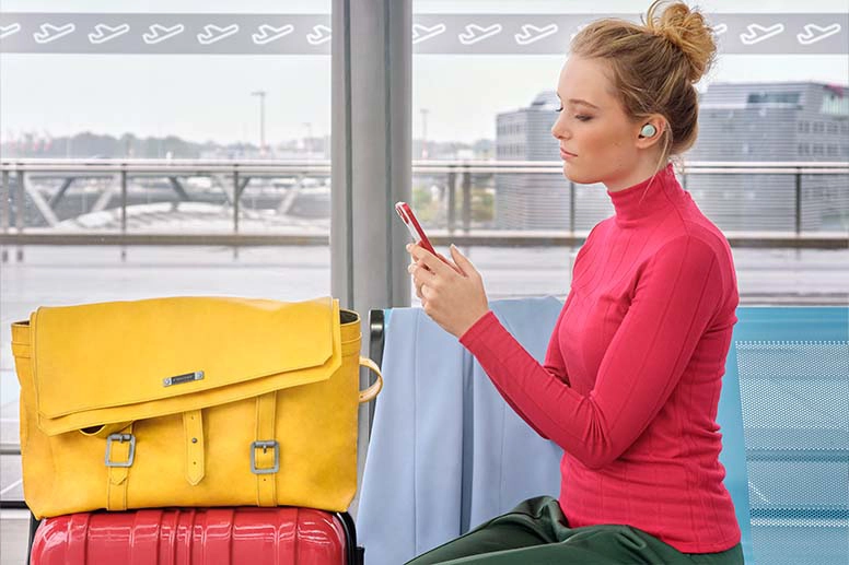 Person mit Bluetooth-Kopfhörer hält ein Smartphone in der Hand.