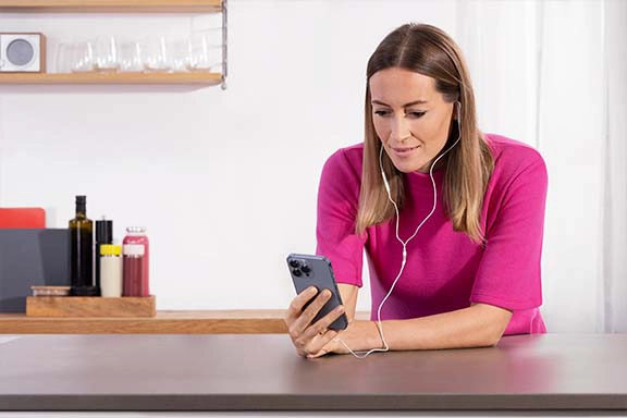 Person hat kabelgebundene Earbuds im Ohr und ein Handy in der Hand.