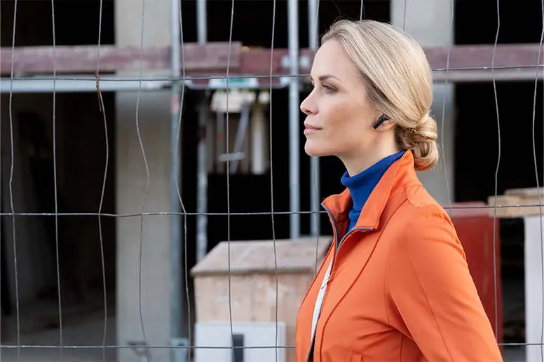 Person vor einer Baustelle mit In-Ear-Kopfhörern.