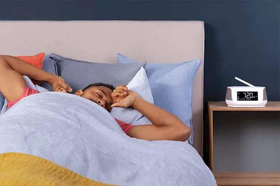 Person im Bett, die gerade vom Radiowecker geweckt wird.