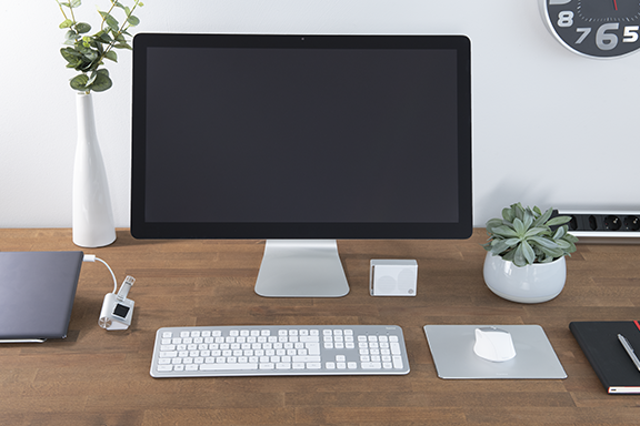 Auf einem Holztisch ist ein PC-Arbeitsplatz eingerichtet mit Monitor, Tastatur, Laptop und einer Maus, die auf dem Hama Mauspad aus Aluminium liegt
