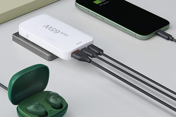 Auf einem Schreibtisch liegen das Hama Schnelladegerät mit 65 Watt, ein Smartphone, Tablet und Bluetooth-Kopfhörer, die gleichzeitig über den Mini-Schnelllader geladen werden.