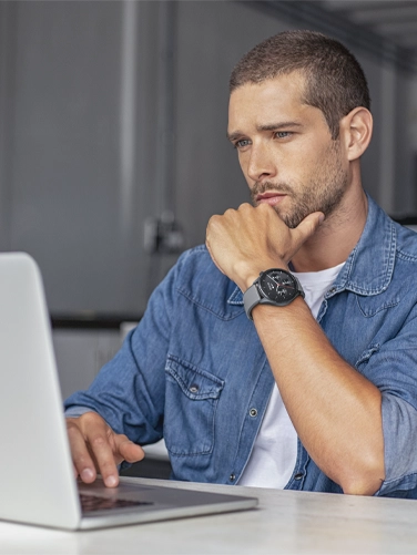 Ein Mann arbeitet mit seiner Smartwatch am Arm an seinem Laptop im Büro