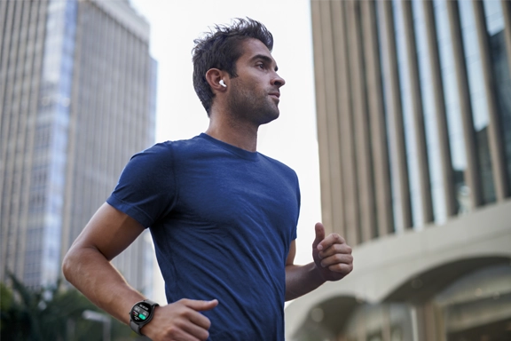 Mann joggt mit Kopfhörern im Ohr und Smartwatch an der Hand durch die Stadt