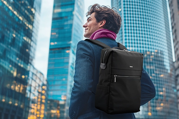 Ein junger Mann steht in einer Großstadt mit modernen Hochhäusern. Auf dem Rücken trägt er den Laptop-Rucksack "Ultimate"