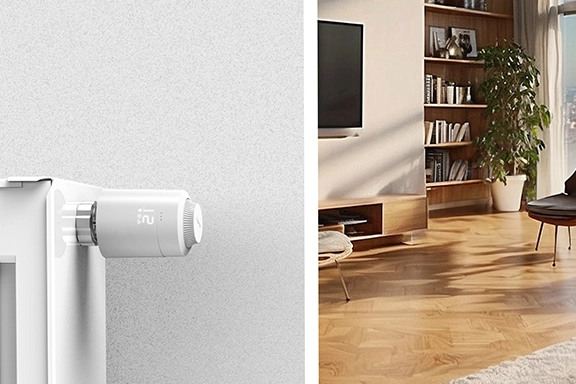 Auf der linken Seite des Bildes sieht man den Hama Thermostat an einem Heizkörper direkt an der Wand. Im Hintergrund einen gemütlich eingerichteten Wohnraum.